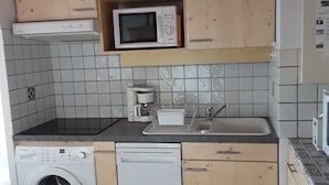 Et lille køkken med træskabe, en mikrobølgeovn, en vaskemaskine og en opvaskemaskine.