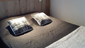 En seng med to puder, et træpanelfag, et billede i ramme på væggen og en lampe monteret på væggen.