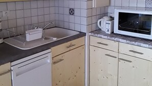 Et køkken med hvide hårde hvidevarer, en vask og flisebeklædte vægge.