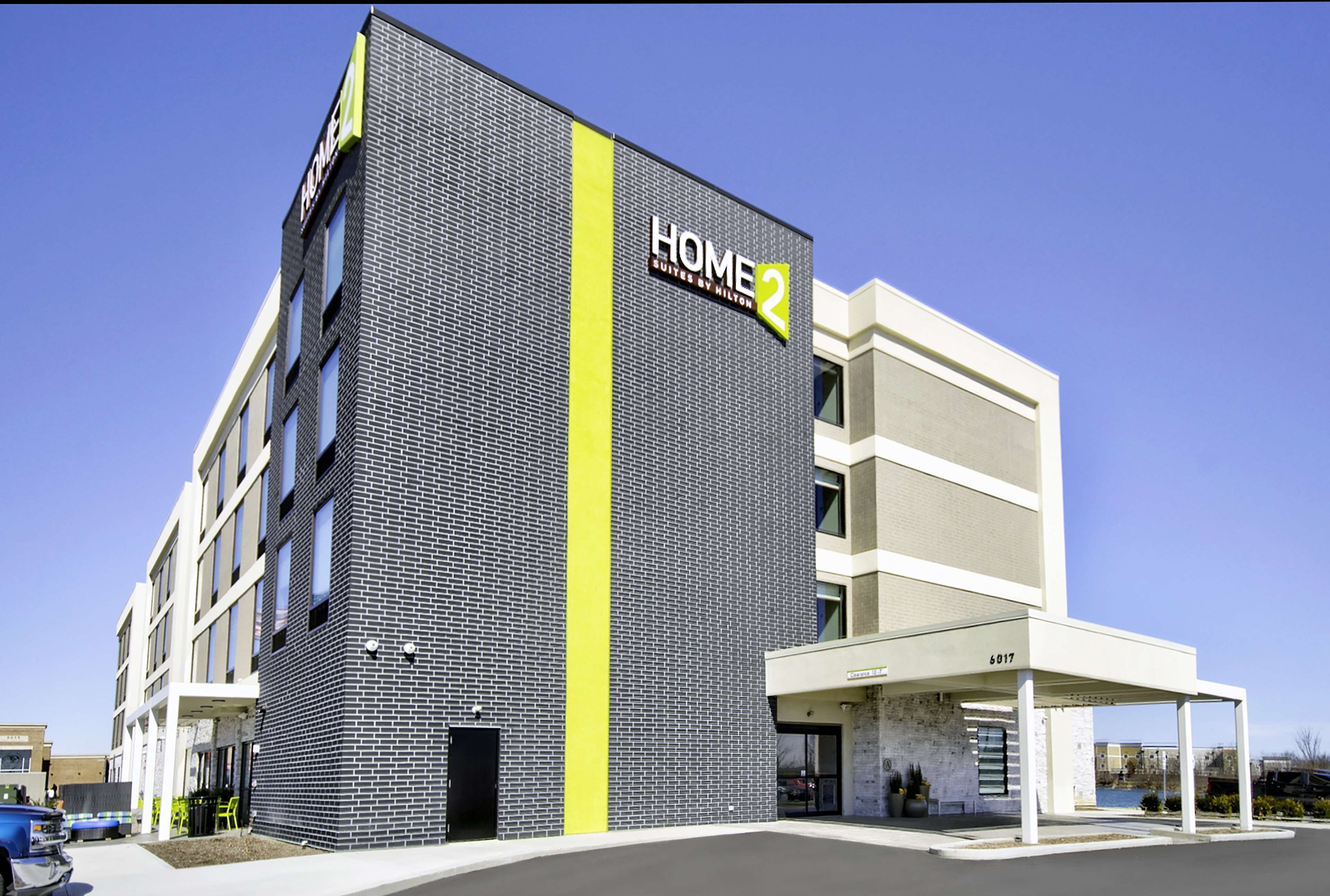 A modern hotel with a prominent "HOME 2" sign, a brick facade, and a covered entrance area.