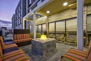 An outdoor seating area with a fire pit, cushioned seating, and a stone wall backdrop.