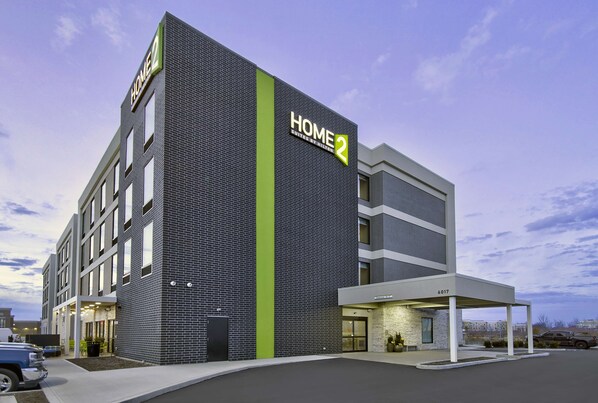 A modern hotel with a prominent "HOME 2" sign, a covered entrance, and a parking area.