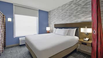 Quarto de hotel com uma cama grande, mesa de cabeceira com telefone, janela com cortinas e parede com padrão texturizado.