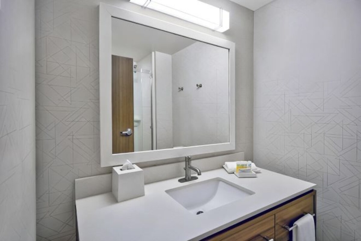 Un baño con un espejo grande, un lavabo, un perchero para toallas y una caja de pañuelos.