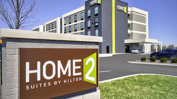 A hotel sign for Home 2 Suites by Hilton, indicating a modern building with a clear sky and a parking lot.