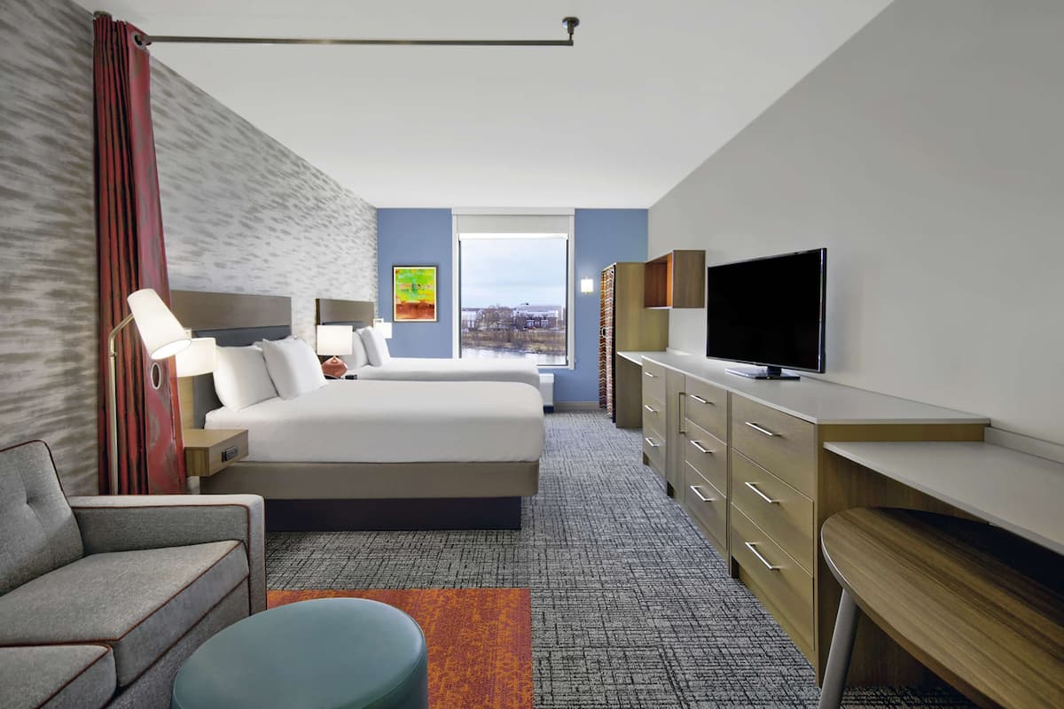 Habitación de hotel con cama, escritorio, televisor y vista a la ciudad.