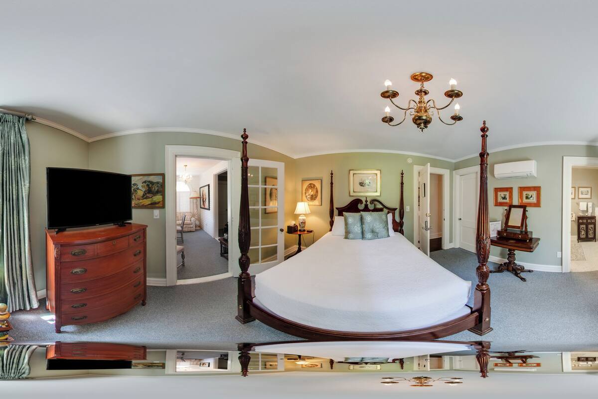 A bedroom with a four-poster bed, a dresser, a vanity, and a window with a view.