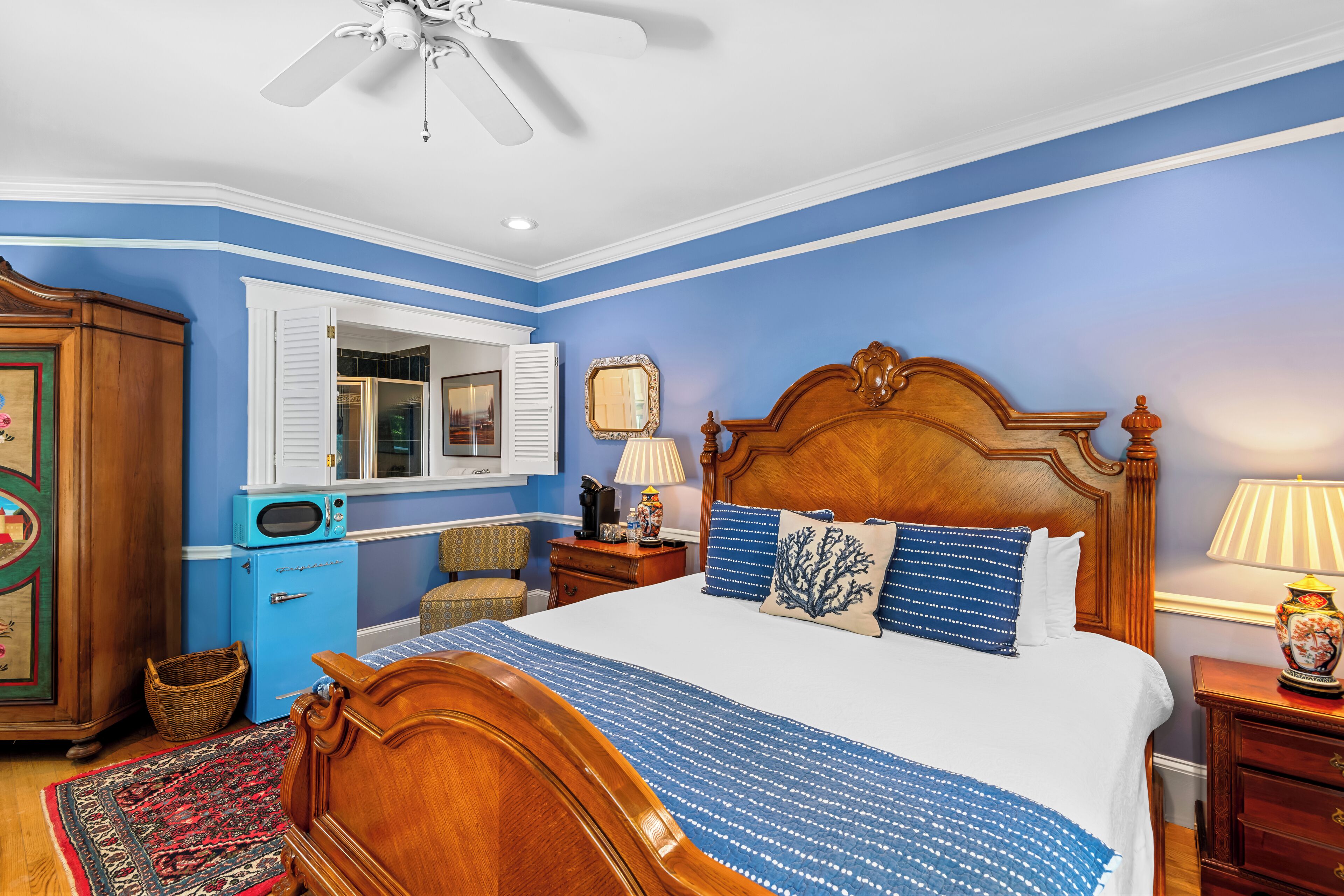 A bedroom with a wooden bed, a blue wall, a ceiling fan, and a small blue refrigerator.