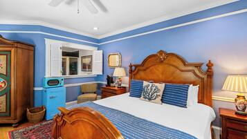 A bedroom with a wooden bed, a blue wall, a ceiling fan, and a small blue refrigerator.