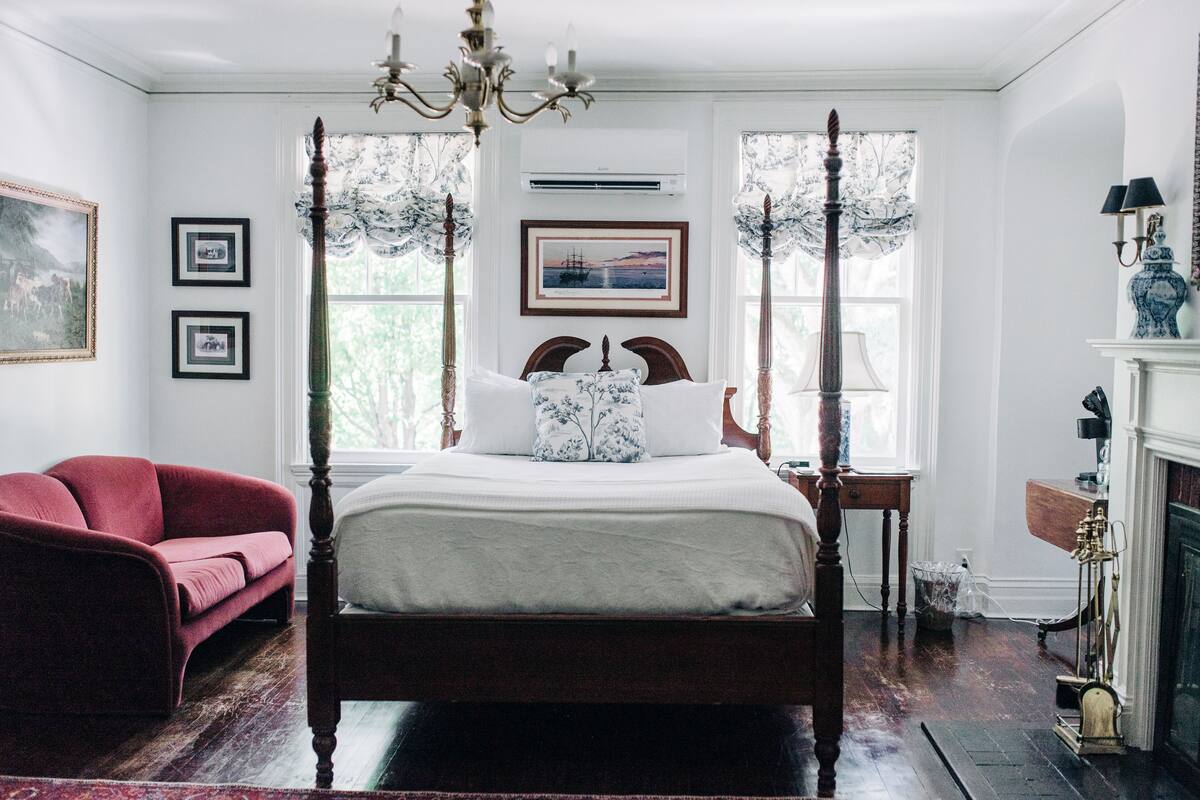 A traditional bedroom with a four-poster bed, a red sofa, and a fireplace.
