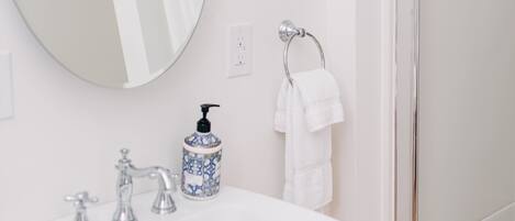 A bathroom with a white sink, a round mirror, a shower, and a towel rack.