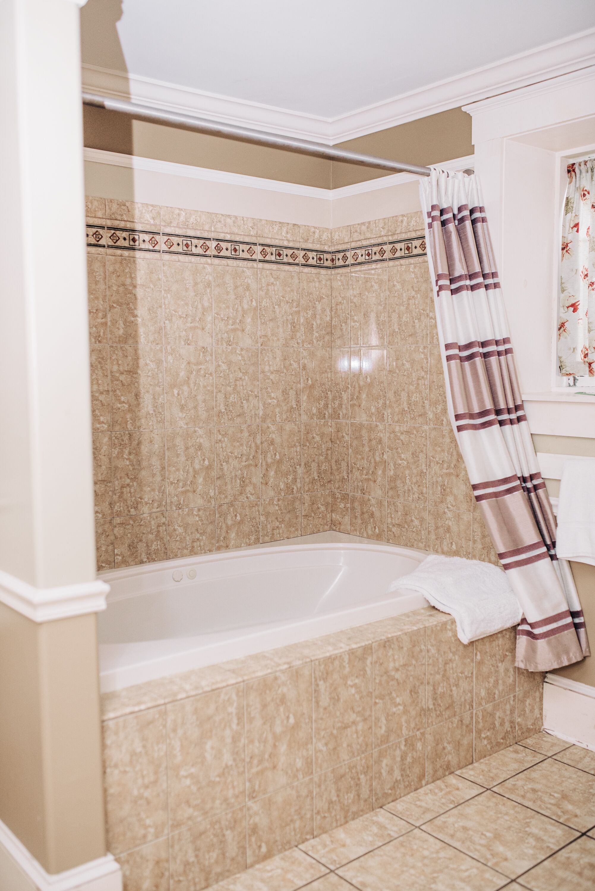 Un baño con bañera, paredes de azulejos color beige y cortina de ducha a rayas.