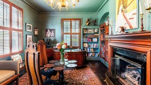 Ein Zimmer mit Kamin, Bücherregalen, einem Chandelier und einem großen Fenster mit Jalousien.