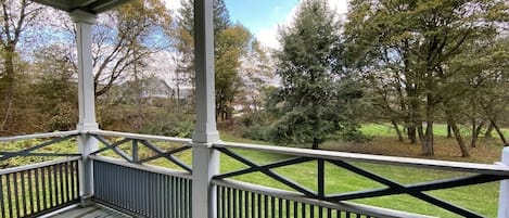 A covered porch with a view of a grassy area and trees.