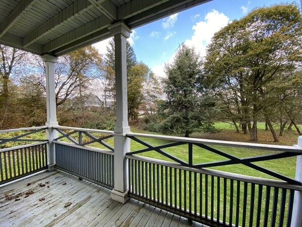A covered porch with a view of a grassy area and trees.