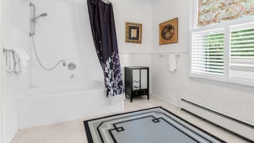 A bathroom with a bathtub, shower, and a small side table.