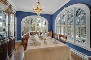 A dining room with a long table set for a meal, large arched windows, and a chandelier.