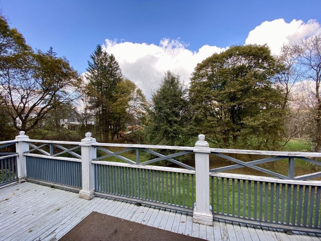 Een houten terras met witte relingen met uitzicht op een gazon met bomen.