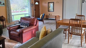 A living room with a red leather sofa, a grey sofa, a wooden dining table with chairs, and a view of the outdoors through a window. - Olympic  Adventure Home, Your Gateway To Adventure And Olympic National Park (Port Angeles)