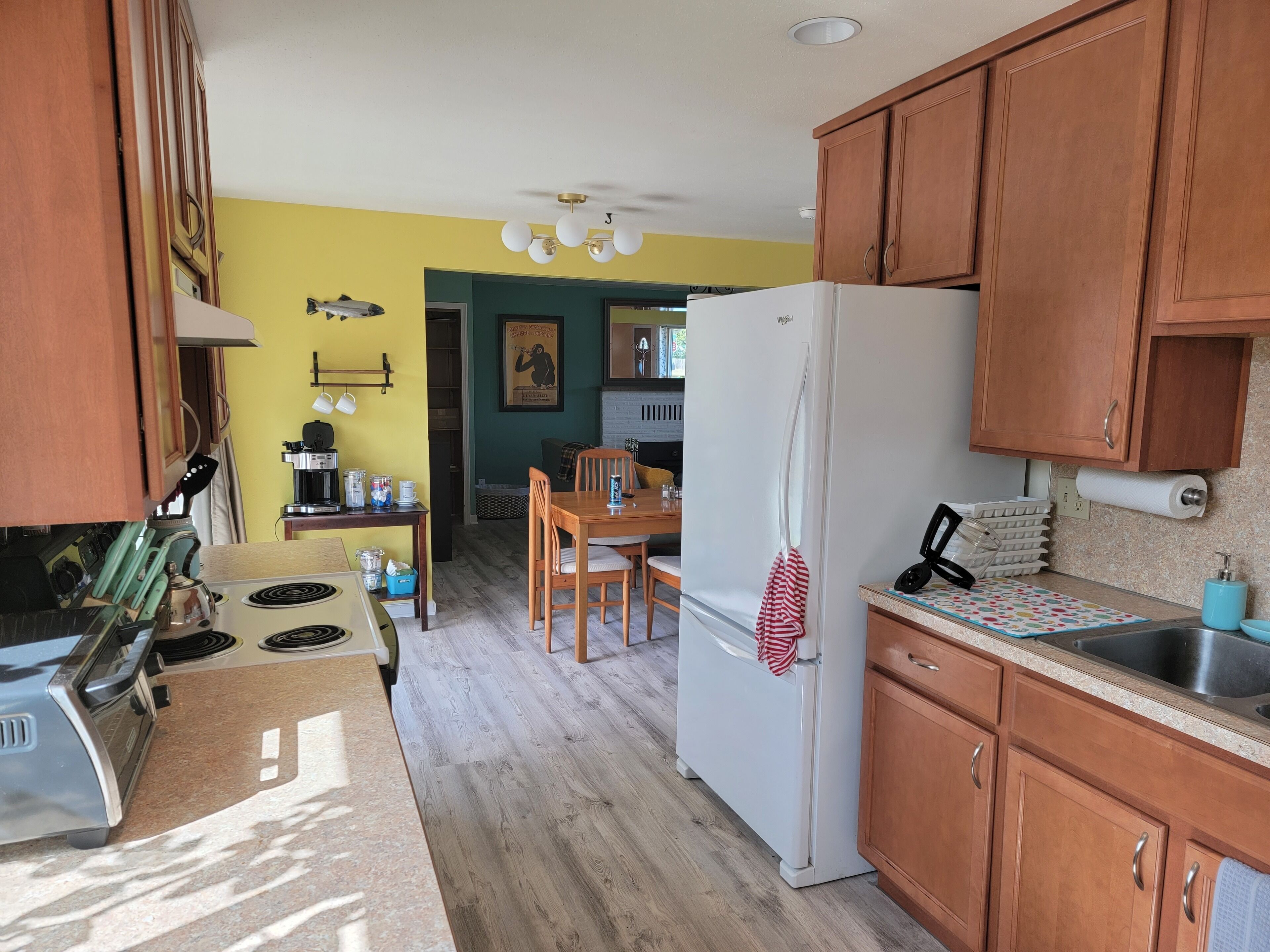 A compact kitchen with wooden cabinets, a white refrigerator, a coffee machine, and a dining area with a table and chairs.
