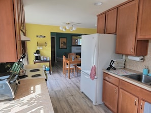 A compact kitchen with wooden cabinets, a white refrigerator, a coffee machine, and a dining area with a table and chairs.