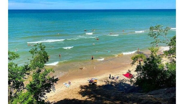 Une plage avec une eau cristalline, des gens qui se baignent et des parasols sur le sable.