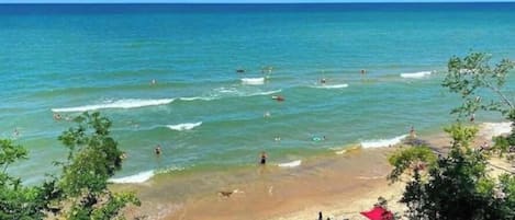 A beach with clear water, people swimming, and umbrellas on the sand.