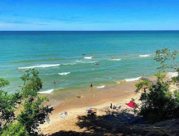 Una playa con agua azul cristalina, gente nadando y una orilla arenosa con árboles.