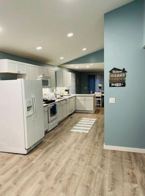 Una cocina moderna con armarios blancos, horno empotrado y microondas. Hay una alfombra a rayas en el piso y un letrero en la pared que dice 'Welcome to the Lake House'.