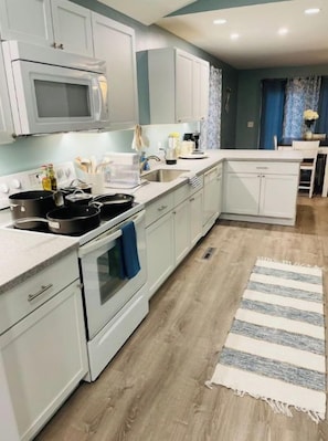 Una cocina moderna con armarios blancos, un microondas, estufa y lavabo.