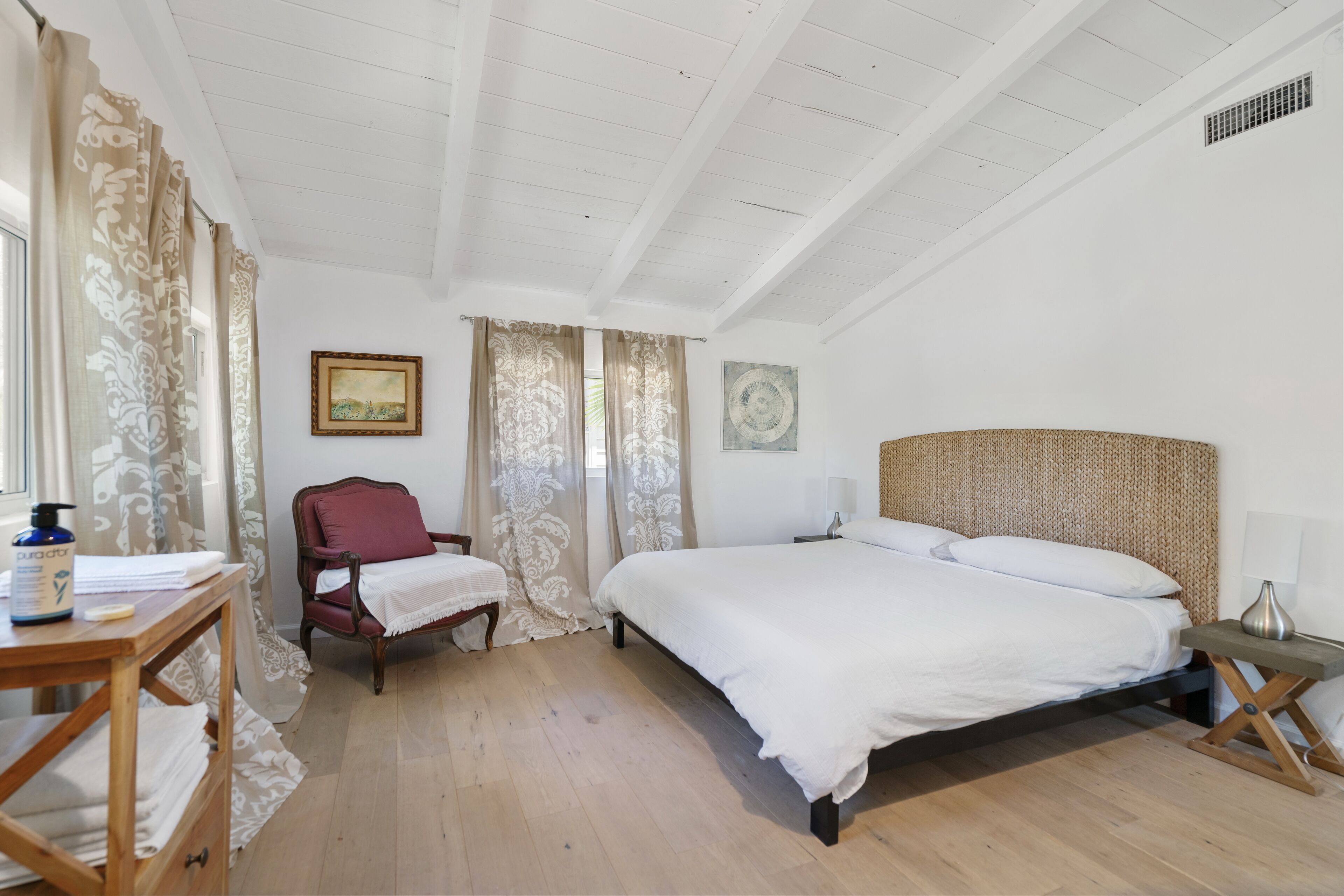 A bedroom with a large bed, a wooden nightstand, a chair, and a table with towels and toiletries.