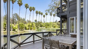 A wooden deck with a table and chairs overlooking a lake with palm trees. - Pitchouline Estate @ Vineyard & Olive Grove by Fallbrook, Temecula Wine County (Fallbrook)