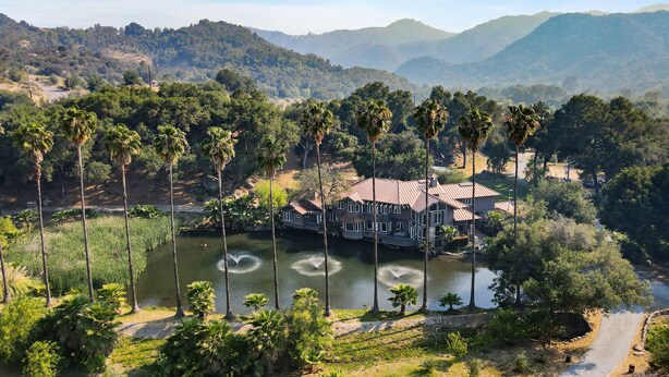 A large house with a pond in front, surrounded by palm trees and hills in the background. - Pitchouline Estate @ Vineyard & Olive Grove by Fallbrook, Temecula Wine County (Fallbrook)