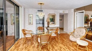 A dining area with a glass table surrounded by wicker chairs, a chandelier, and a mirror above the table. - Anchorage 204 (Siesta Key)
