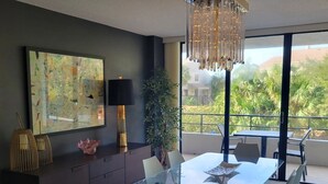 A modern dining area with a glass table, metal chairs, a chandelier, a large abstract painting, a floor lamp, and a potted plant. - Anchorage 211 in Siesta Key (Siesta Key)