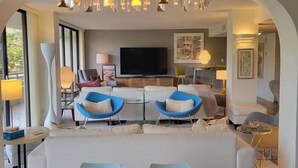 A modern living room with a large TV, two blue armchairs, a sofa, and a chandelier. - Anchorage 211 in Siesta Key (Siesta Key)