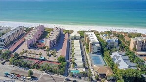 Luftaufnahme eines Küstenhotels mit mehreren Gebäuden, einem Strand und einem Parkplatz.