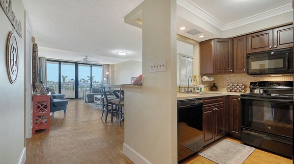 A spacious living area with a dining table and chairs, a kitchen with dark wooden cabinets and modern appliances, and a large sliding glass door leading to a balcony with a view. - Anchorage 405 (Siesta Key)