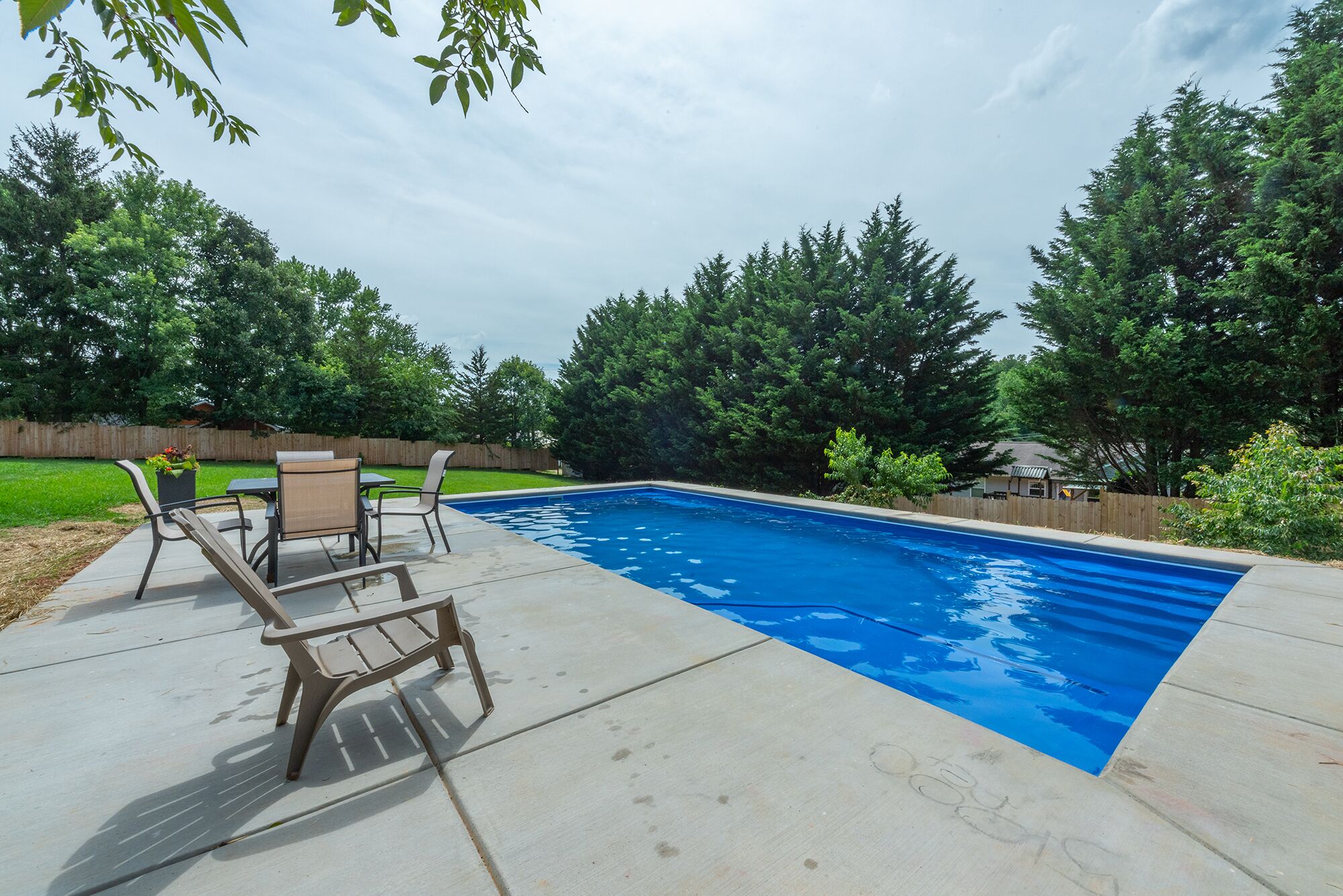 Une piscine rectangulaire avec une terrasse en bois et des chaises.