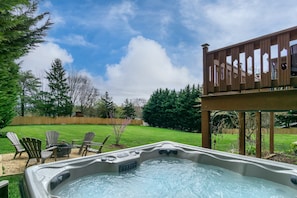 A hot tub in a backyard with a wooden deck and outdoor furniture. - 8-minutes to Downtown! Pool, Hot Tub, Game Room, Theater | Bathrooms en-suite (Asheville)