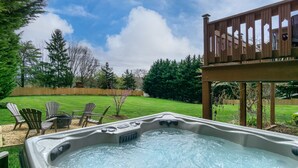 Uma banheira de hidromassagem em um quintal com deck de madeira, gramado verde e móveis de jardim.