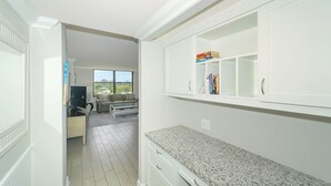 Eine moderne Küche mit weißen Schränken, einer Granitarbeitsplatte und Blick zu einem Wohnbereich mit Sofa und Fernseher.