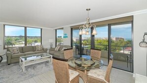 Ein modernes Wohnzimmer mit einem Glastisch, Korbstühlen, einer Couch und großen Fenstern mit Blick auf die Stadt.