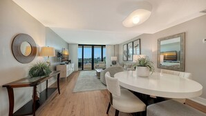 A modern living room with a round dining table, a sofa, and a large window offering a view of the outdoors. - Anchorage 507 (Siesta Key)