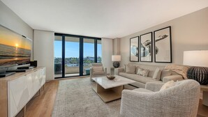 A modern living room with a sofa, armchairs, a coffee table, and a TV on a cabinet. Large windows offer a view of the outdoors. - Anchorage 507 (Siesta Key)