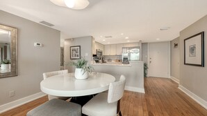 A modern kitchen with white cabinets, a central island, and a dining area with a round table and chairs. - Anchorage 507 (Siesta Key)