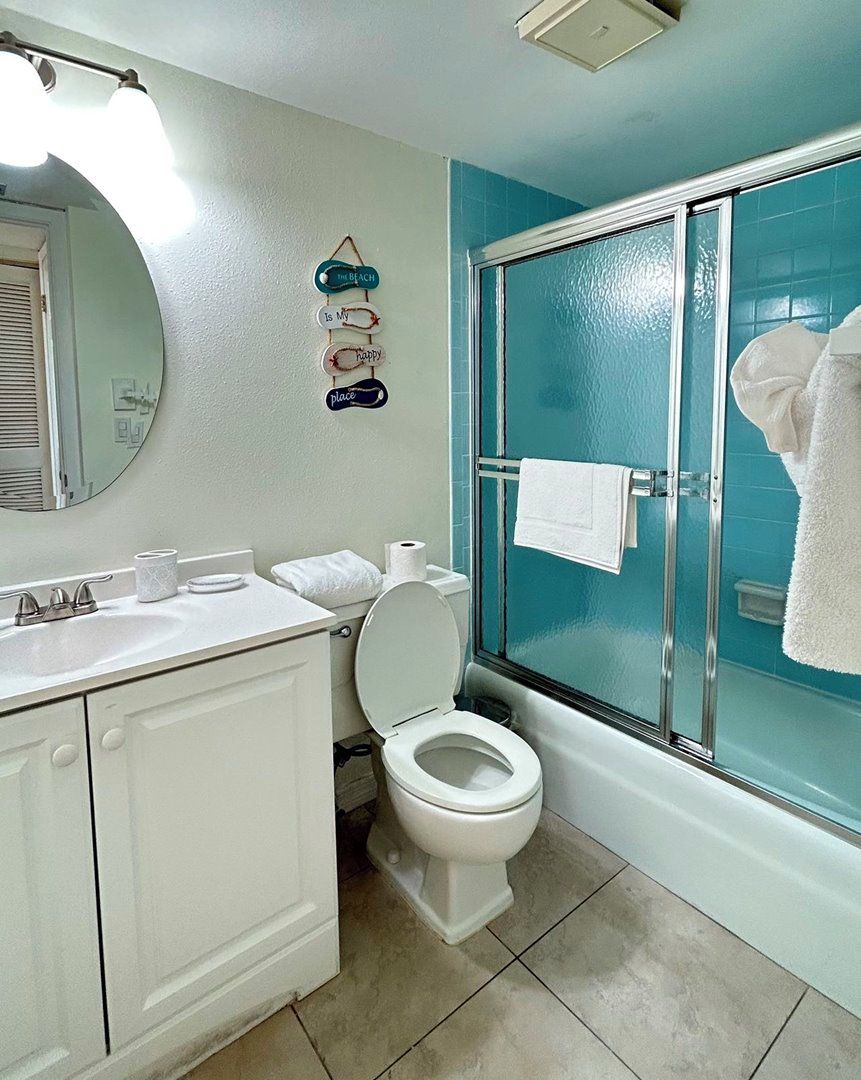 Uma casa de banho com uma sanita branca, uma pia com um espelho em cima e um chuveiro com porta de vidro.