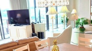 Ett modernt vardagsrum med en brun lädersoffa, ett träbord med vita stolar, en ananas som mittpunkt på bordet och ett stort fönster med gardiner.