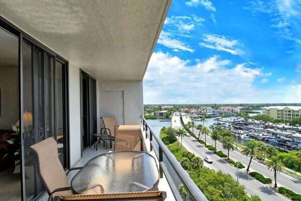 A balcony with a glass table and chairs, overlooking a marina with boats and a road. - Anchorage PH-6 in Siesta Key, FL (Siesta Key)