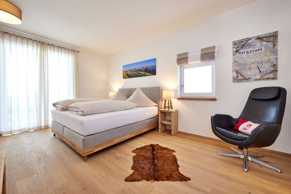A modern bedroom with a bed, a chair, a rug, and a painting on the wall.